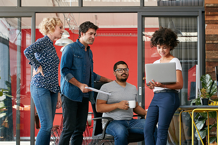 Portrait of group of creative people having a meeting with a laptop in a modern office. Business people having relaxed conversation over new project.