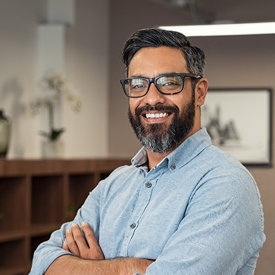 Portrait of happy mature businessman wearing spectacles and looking at camera. Multiethnic satisfied man with beard and eyeglasses feeling confident at office. Successful middle eastern business man smiling in a creative office.